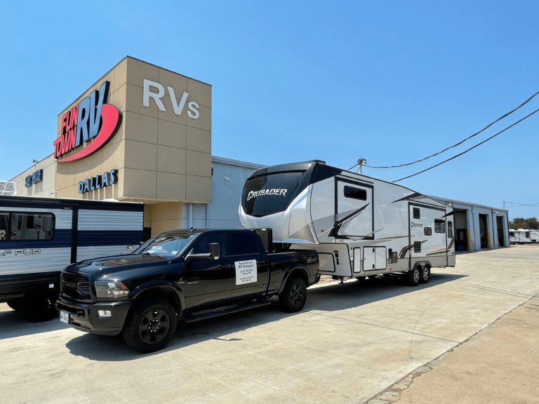 Large fifth wheel RV hitched to transport truck for interstate delivery.