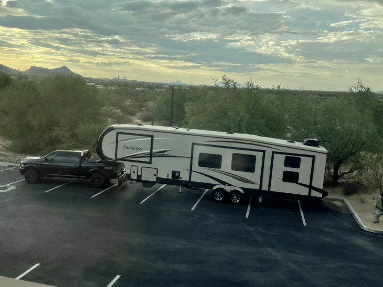 Large fifth wheel RV hitched to transport truck for interstate delivery.